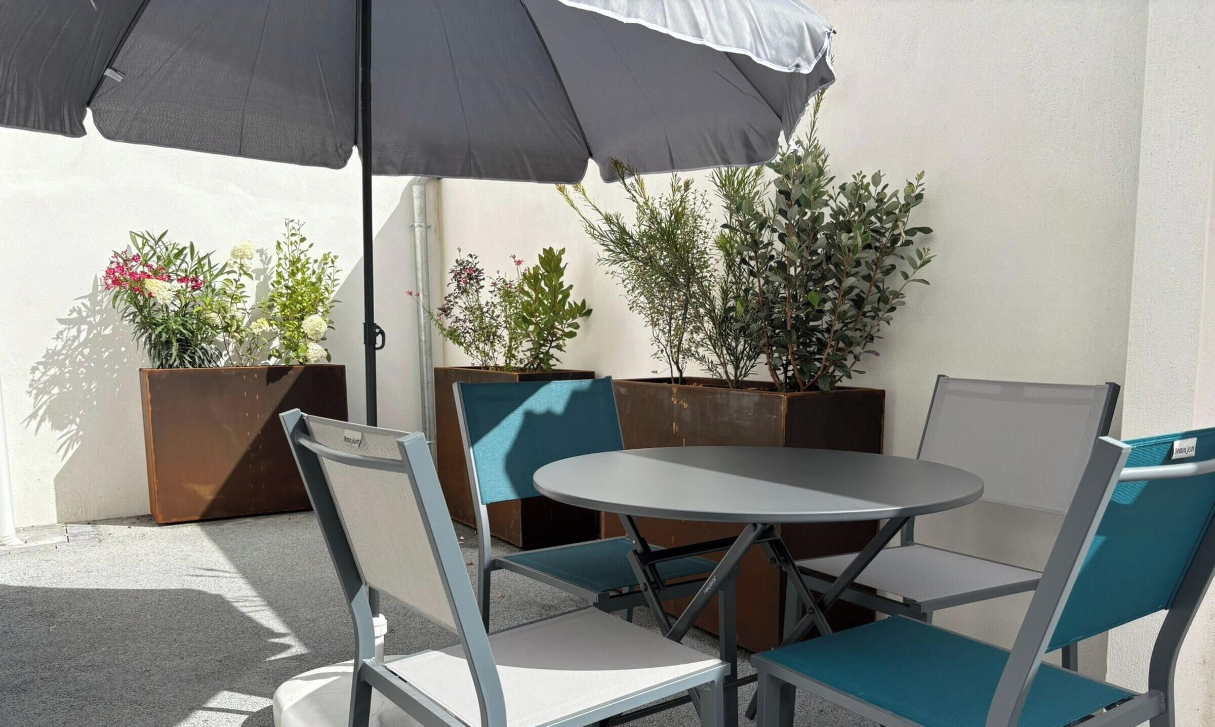 Un espace extérieur aménagé avec une table ronde et des chaises, un parasol et des plantes en pot.