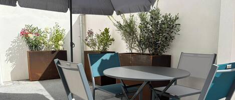 Un espace extérieur aménagé avec une table ronde et des chaises, un parasol et des plantes en pot.