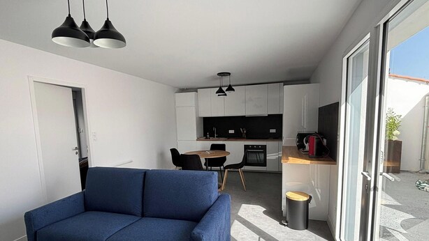 Ein modernes Interieur mit einer Couch, einem Esstisch, einer Küchenzeile und einer Glastür, die zu einem Außenbereich führt.