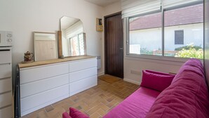 A room with a white dresser, a mirror, a window with blinds, a pink sofa, and a door. - Charming studio at forest edge - 2 guests (Lit-et-Mixe)