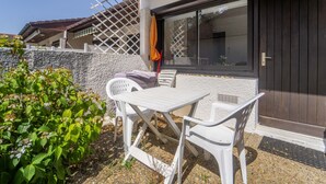 A patio with a table and chairs, a wooden door, and a window. - Charming studio at forest edge - 2 guests (Lit-et-Mixe)