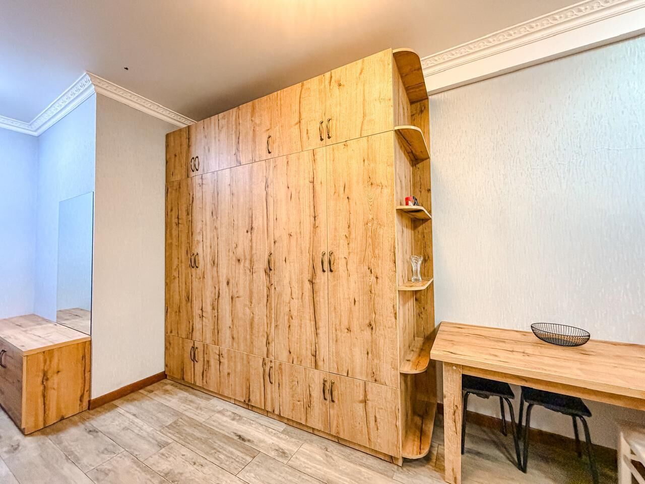 Een kamer met een houten garderobe, een tafeltje met stoelen en een plank met spullen.