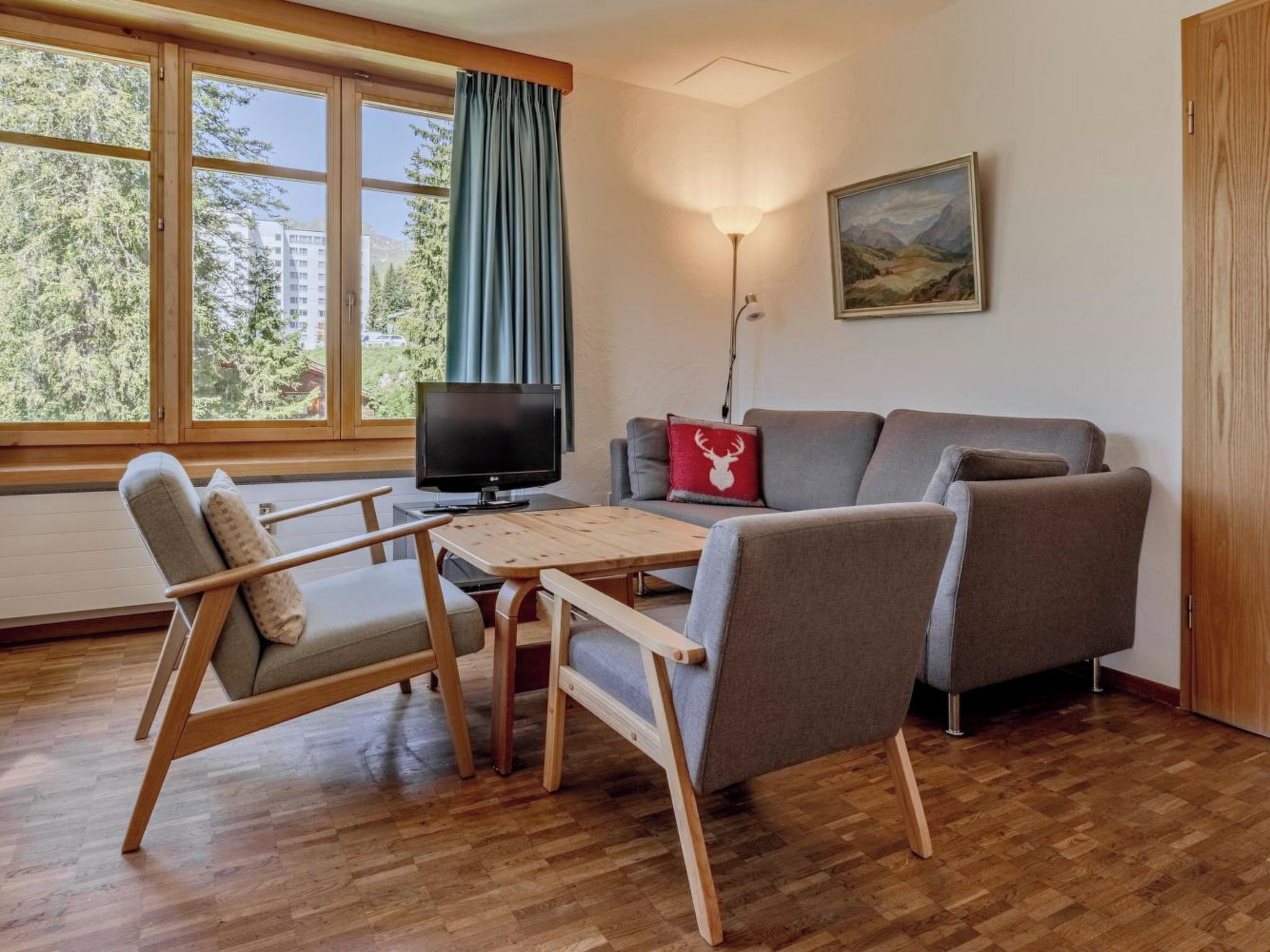 Olohuoneessa on puinen pöytä, kaksi tuolia, sohva, televisio ja seinällä taulu.