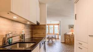 Uma cozinha moderna com bancada preta, painel atrás do fogão em madeira e um espaço de jantar com mesa e cadeiras.