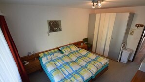 A bedroom with a bed, a nightstand, a dresser, a mirror, and a ceiling light fixture. - Gentiana C-7 Appartement/Fewo, Dusche und Bad, WC, 2-Bettwohnung by Interhome (Arosa)