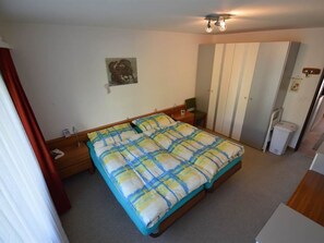 A bedroom with a bed, a nightstand, a dresser, a mirror, and a ceiling light fixture. - Gentiana C-7 Appartement/Fewo, Dusche und Bad, WC, 2-Bettwohnung by Interhome (Arosa)