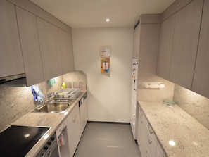 Una cocina funcional con un lavamanos de acero inoxidable, estufa y microondas. Hay un reloj en la pared y un refrigerador pequeño.