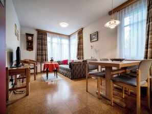 A modern living room with a sofa, dining table, chairs, a TV, and a clock on the wall. - Tschuggenweg 2 Appartement/Fewo, Bad, WC, 2-Bettwohnung 2-Bettwohnung by Interhome (Arosa)