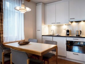 A compact kitchen with white cabinets, a dining table with chairs, a coffee maker, and a kettle. - Tschuggenweg 2 Appartement/Fewo, Bad, WC, 2-Bettwohnung 2-Bettwohnung by Interhome (Arosa)