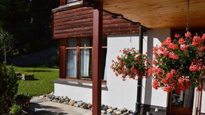 Una casa de madera con base de piedra, un porche y un arreglo floral colgante.