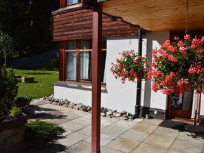 A wooden house with a stone foundation, a porch, and a hanging flower arrangement. - Tschuggenweg 2 Appartement/Fewo, Bad, WC, 2-Bettwohnung 2-Bettwohnung by Interhome (Arosa)