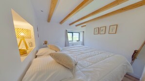 A bedroom with a large bed, wooden beams, a window, and framed pictures on the wall. - Cozy T2 apartment with terrace - 2 guests (BOIS D'AMONT)