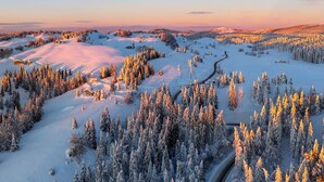A snowy landscape with a winding road, dense forest, and distant hills. - Cozy T2 apartment with terrace - 2 guests (BOIS D'AMONT)