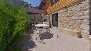 A patio with a round table and chairs, surrounded by a stone wall and greenery. - Cozy T2 apartment with terrace - 2 guests (BOIS D'AMONT)