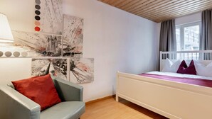 Un dormitorio con una cama, una silla y obras de arte en la pared.