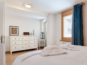 A bedroom with a bed, a dresser, a framed picture, a window with curtains, and a radiator. - SKA Haus Appartement/Fewo, Dusche und Bad, WC, 6-Bettwohnung by Interhome (Arosa)