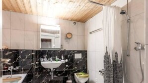 Un baño con tocador de mármol, inodoro, ducha con cortina y techo de madera.