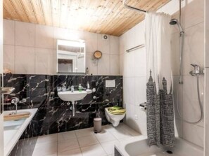 Ein Badezimmer mit Marmorwaschtisch, Toilette, Duschkabine mit Vorhang und Holzboden.