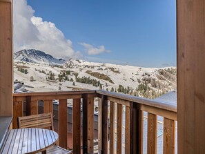 A wooden deck with a table and chair, overlooking a mountainous landscape with snow-covered slopes and a clear sky. - Spacious apartment, close to slopes - 6 guests (Belle Plagne)