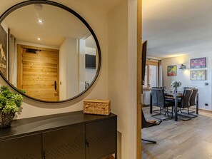 Un intérieur moderne agrémenté d’un grand miroir rond, d’une porte en bois, d’un coin repas avec une table et des chaises, et d’œuvres d’art accrochées aux murs.