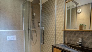 Ein modernes Badezimmer mit einer Glasdusche, einem Holzkosmetikschrank und einem Spiegel.
