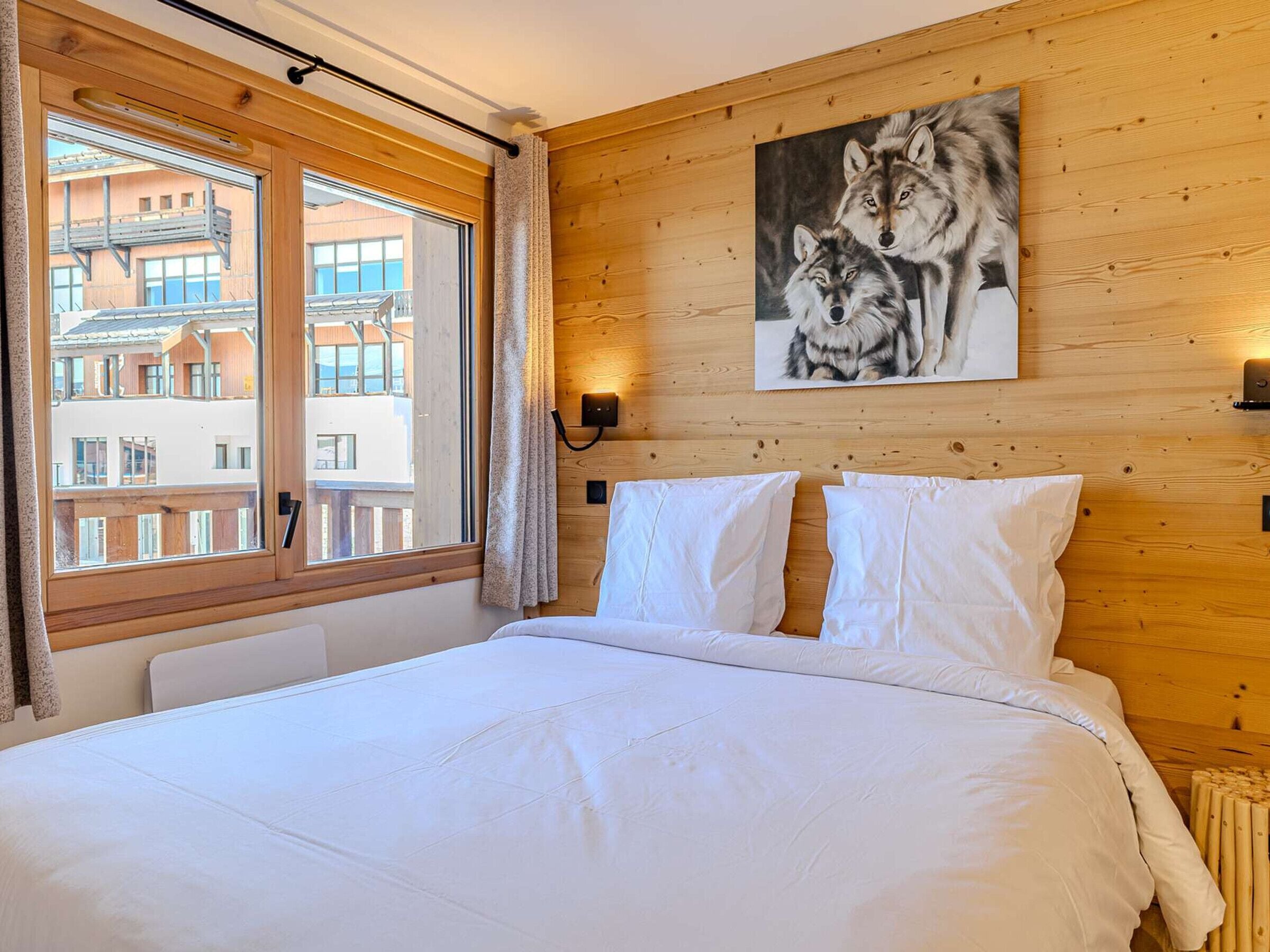 Habitación de hotel con una cama grande, paredes de madera, una ventana con cortinas y un cuadro de lobos.