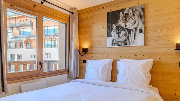 Ein Hotelzimmer mit einem großen Bett, Holzwänden, einem Fenster mit Vorhängen und einem Bild von Wölfen.