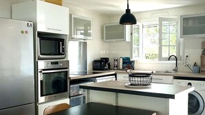 Eine moderne Küche mit Edelstahlgeräten, einer zentralen Kochinsel mit Sitzgelegenheiten und Blick ins Freie.