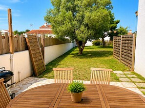 Terrassa de fusta amb dues cadires, una taula, una planta en test i una barbacoa.