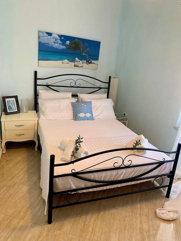 A neatly made bed with white linens, a single decorative pillow, and a framed picture on a bedside table.