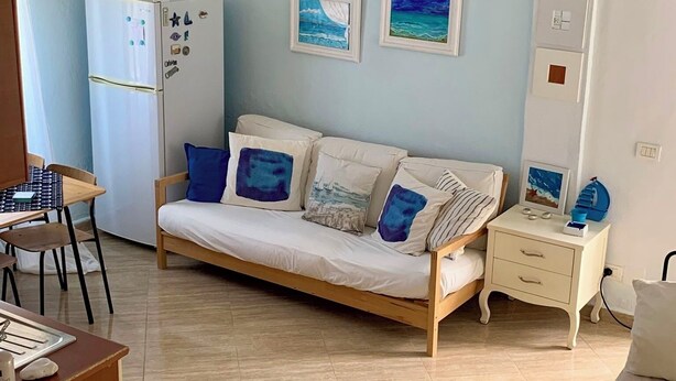 Ett rum med en soffa, ett litet bord, ett skrivbord, en lampa och ett kylskåp.