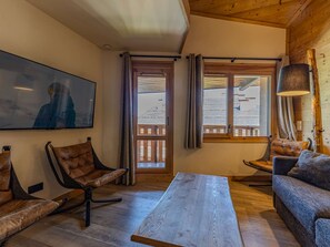 A cozy room with a wooden ceiling, a large window with curtains, a flat-screen TV, leather chairs, and a wooden coffee table. - Central duplex, sauna - 8 guests (Belle Plagne)