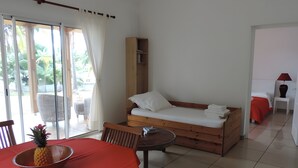 A room with a bed, a dining table with a pineapple, a chair, and a small table. - Villas Manapany – Villa Le Jacquier: 3★ Seaside Comfort in La Réunion (Saint Joseph)