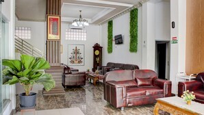 A spacious lobby with a grand staircase, leather sofas, a large potted plant, and a chandelier.