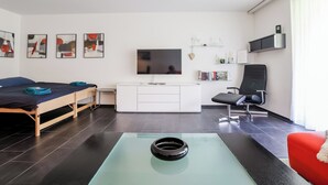 A modern hotel room with a bed, a desk, a chair, a TV, and a bookshelf. - Rothornblick 8 Appartement/Fewo, Bad, WC, 4-Bettwohnung by Interhome (Arosa)