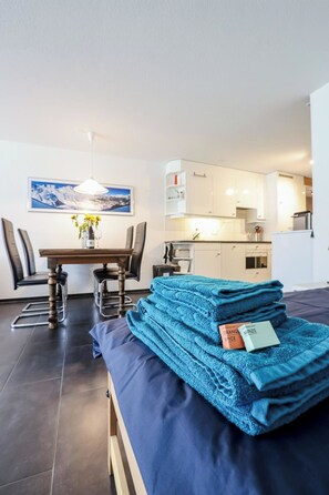 Quarto moderno com cama, mesa de jantar, cadeiras, área de cozinha e um quadro na parede.