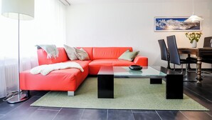 A modern living room with a red sofa, a glass coffee table, and a dining area with a table and chairs. - Rothornblick 8 Appartement/Fewo, Bad, WC, 4-Bettwohnung by Interhome (Arosa)