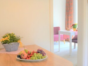 A dining area with a table set for a meal, a potted plant, and a view of a living room with a pink chair and a table. - Bisang S Appartement/Fewo,   4-Bettwohnung by Interhome (Arosa)