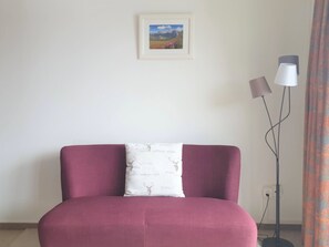 A room with a single red sofa, a white cushion with a nature pattern, a framed landscape picture on the wall, and a floor lamp. - Bisang S Appartement/Fewo,   4-Bettwohnung by Interhome (Arosa)