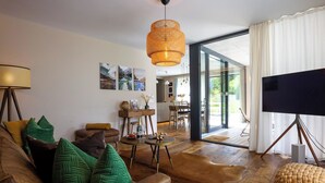 Ein modernes Wohnzimmer mit Sofa, Couchtisch, Fernseher auf einem Schrank und einer Essecke mit Stühlen und Tisch.