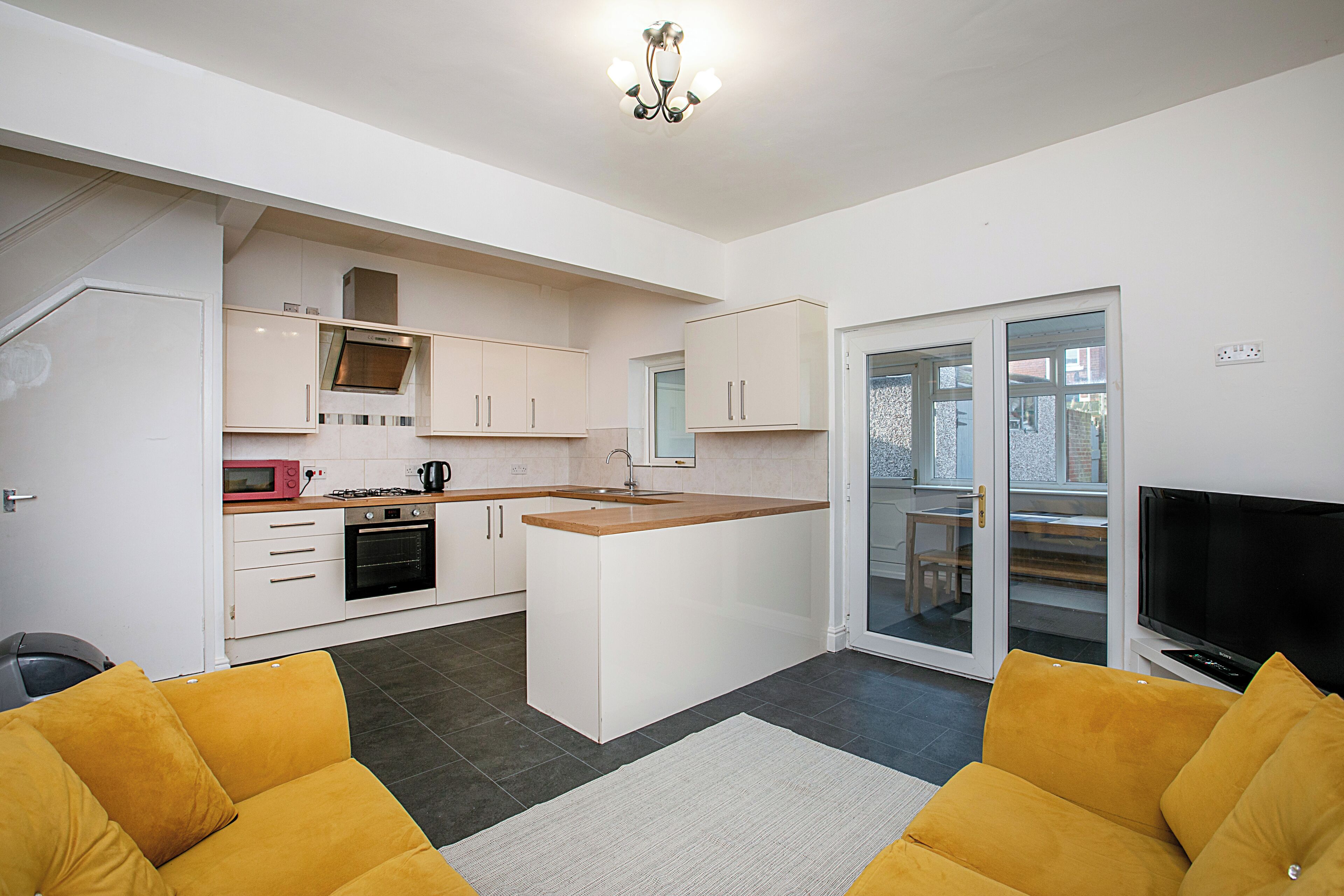 A compact kitchen with white cabinets, a microwave, and a stove. There's a small island with a sink, and a sliding glass door leading to a balcony.