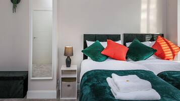 A bedroom with a bed, pillows, a nightstand, a lamp, a mirror, and a small plant.