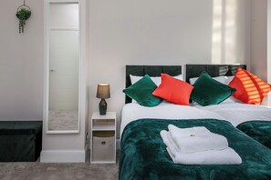 Ein Schlafzimmer mit Bett, Kissen, Nachttisch, Lampe, Spiegel und einer kleinen Pflanze.