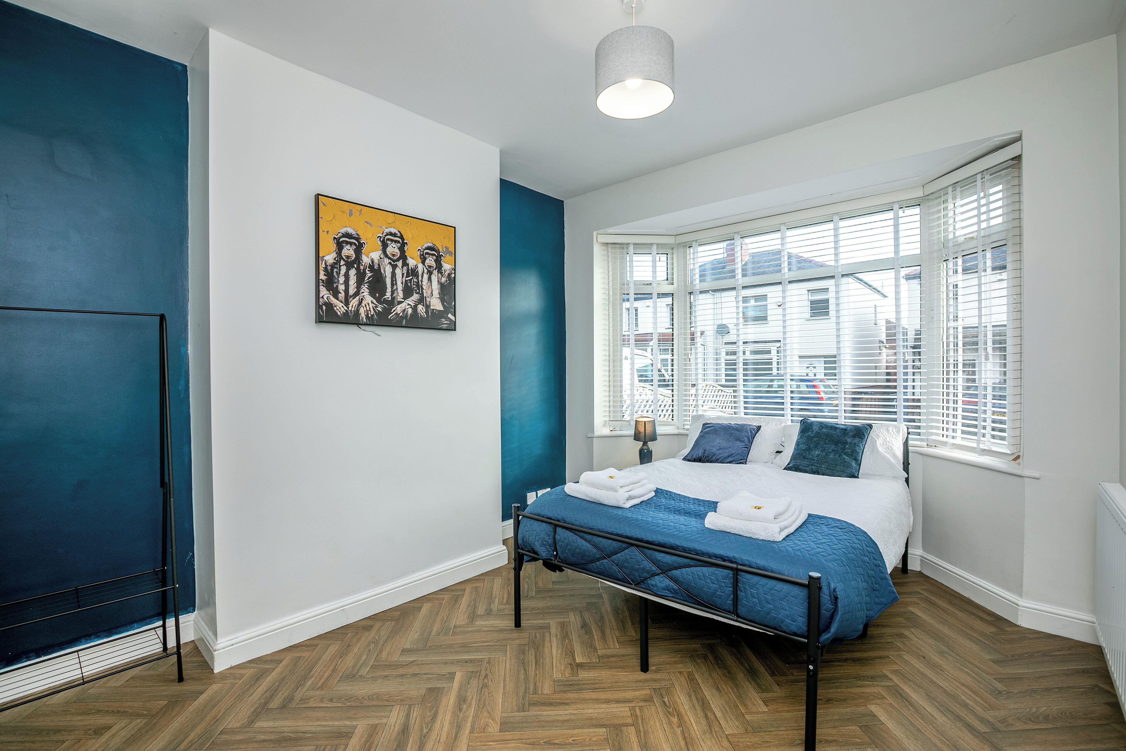 A bedroom with a bed, a window with blinds, a painting on the wall, and a radiator.