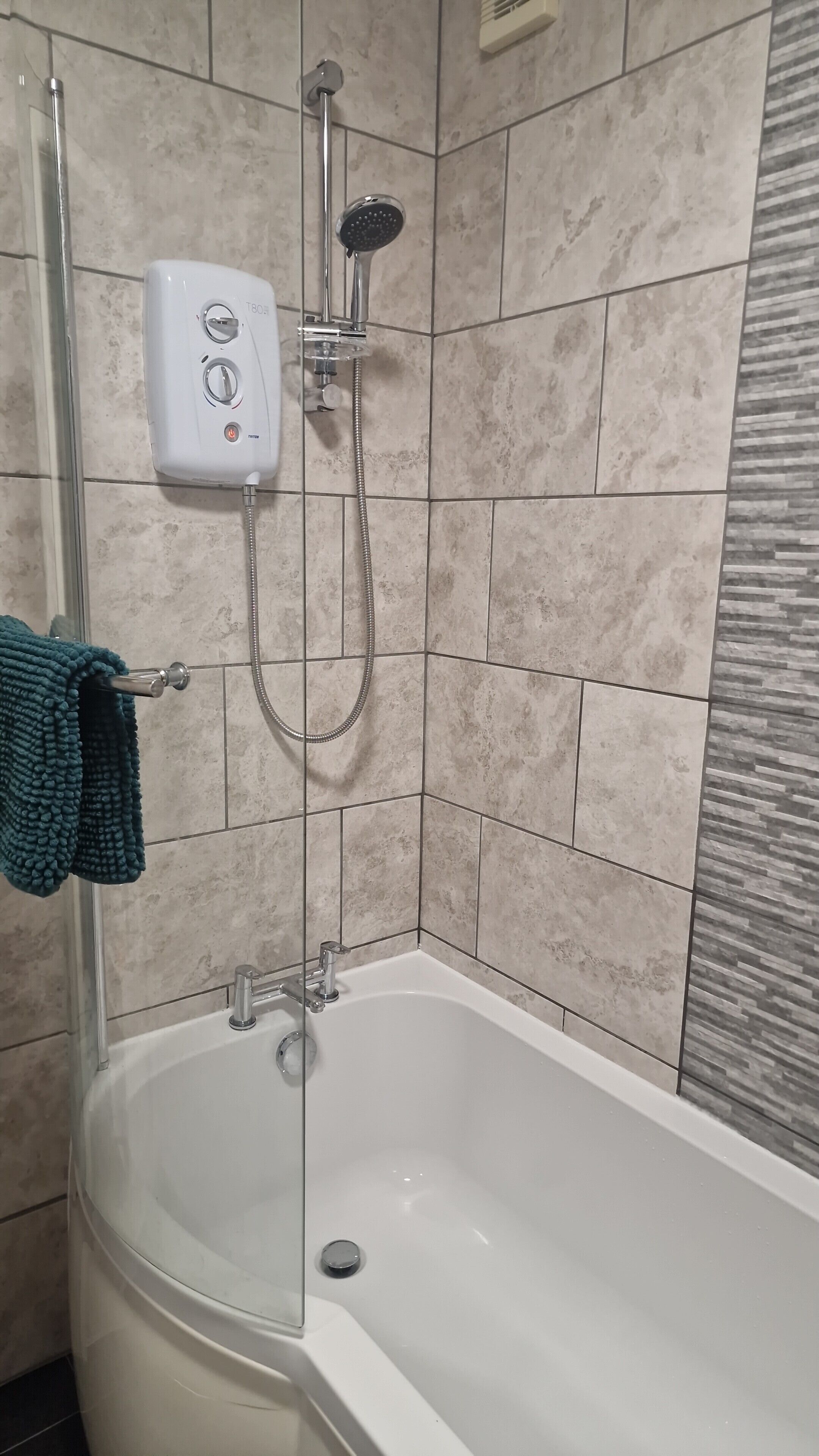 A bathroom with a bathtub, a handheld showerhead, and a wall-mounted control panel.