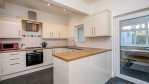 Cocina moderna con armarios blancos, horno empotrado, microondas y ventana con vista a un muro de ladrillo.