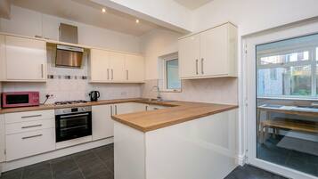 A modern kitchen with white cabinetry, a built-in oven, a microwave, and a window overlooking a brick wall.