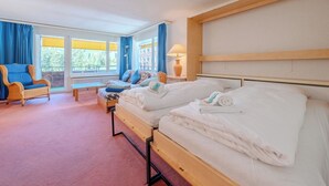 Habitación de hotel con dos camas, una silla, un banco y una ventana con cortinas.