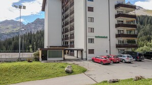Un hotel de varios pisos con techo plano, balcones y un estacionamiento con automóviles.