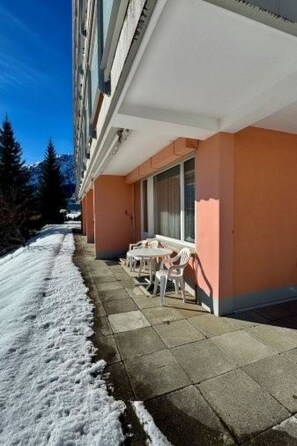 Ein Gebäude mit einer überdachten Außenbestuhlung, verschneitem Gelände und wolkenlosem Himmel.
